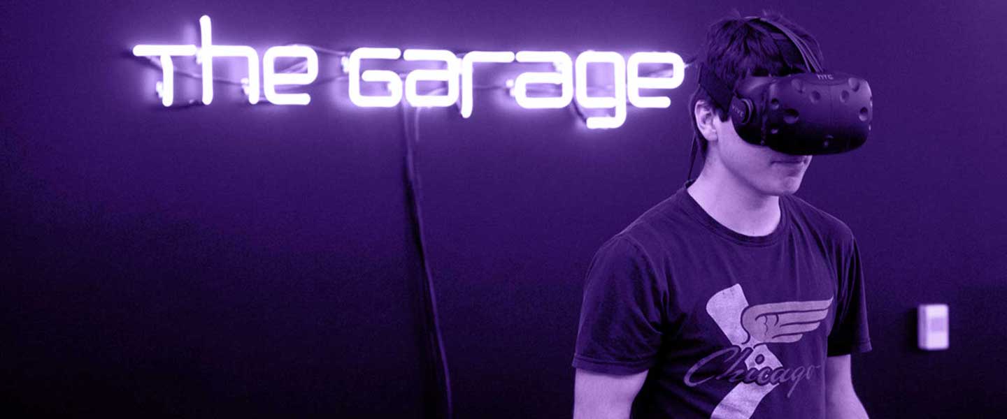 Student using Virtual Reality headset with The Garage sign behind him